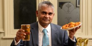Romail Golzar - pint of beer in right hand and onion bargees on a plate in left hand