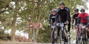 Cyclists riding past Outwoods Woodland Walk brown tourist sign