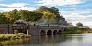 A steam train crossing a bridge by a lake