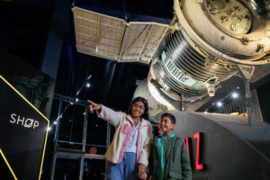 child and mother pointing to the side. There is a space capsule above them